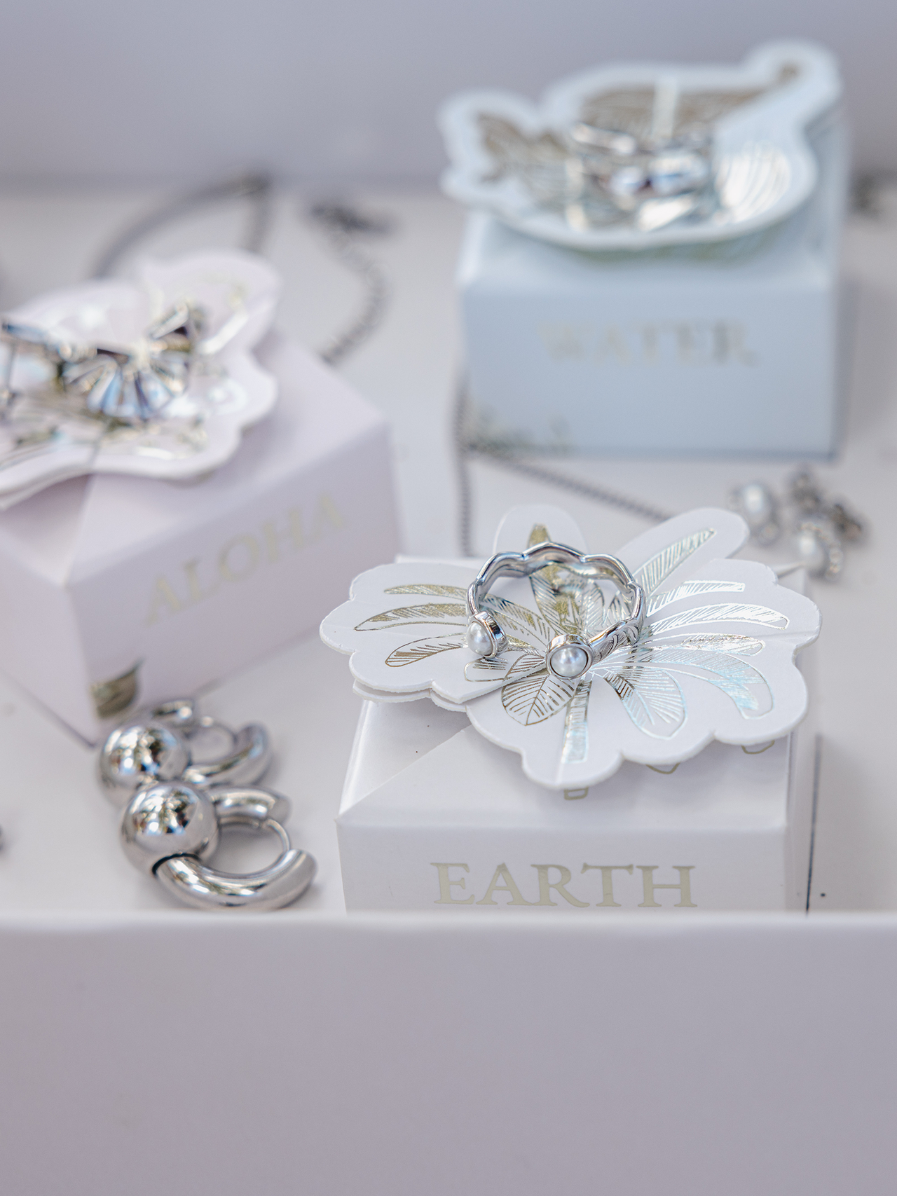 Silberne Schmuckstücke auf zarten Boxen von PURELEI, inspiriert von Aloha und Natur.