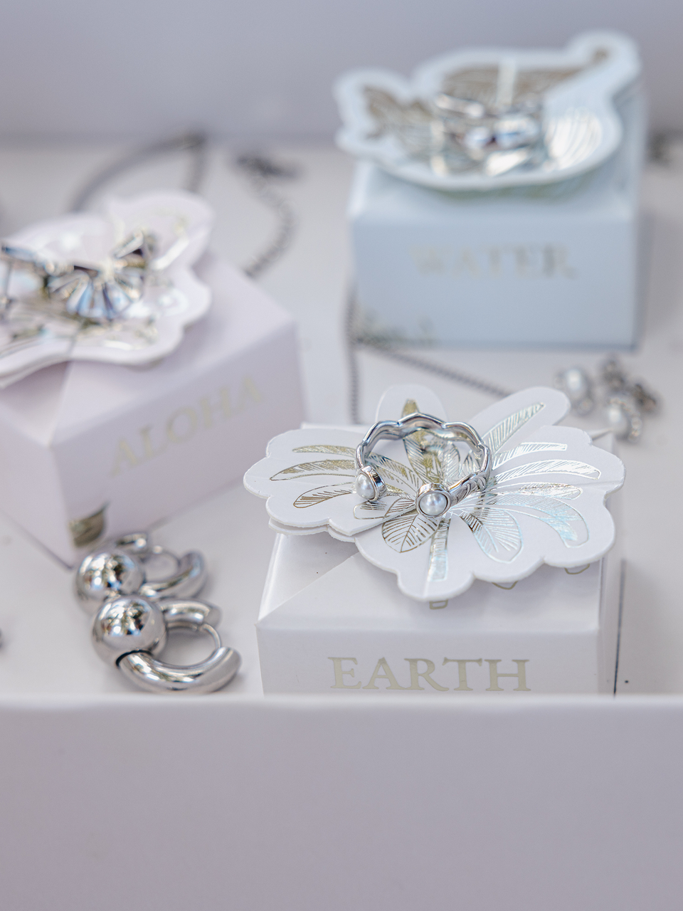 Silberne Schmuckstücke auf zarten Boxen von PURELEI, inspiriert von Aloha und Natur.