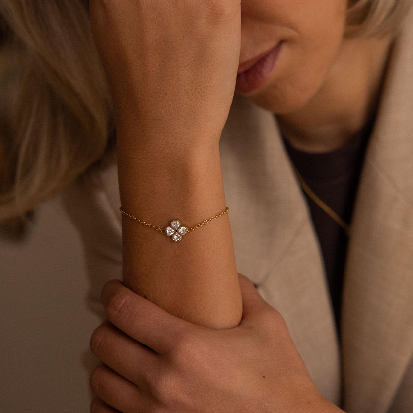 Zartes, goldenes Armband mit floralen Anhängern, getragen am Handgelenk, PURELEI.