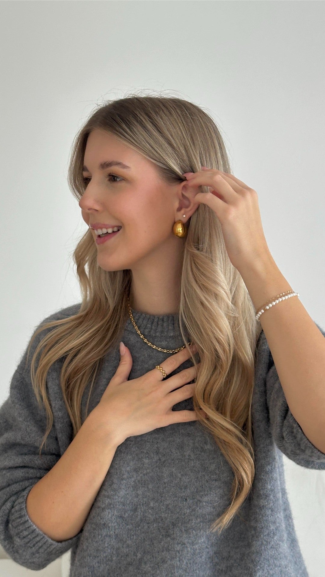 Goldene Creolen und zarte Kette, getragen mit grauem Pullover, PURELEI Stil.