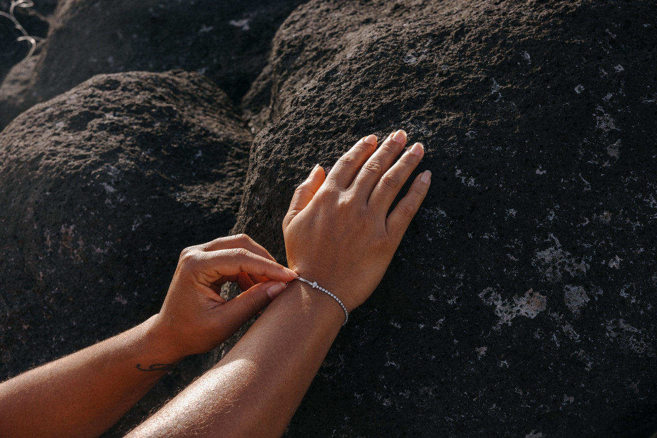 Silbernes Armband mit zarten Perlen, getragen auf einem Handgelenk, umgeben von dunklem Lavagestein – PURELEI.
