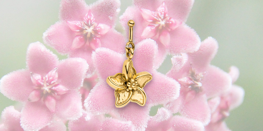 Goldener Blumenanhänger von PURELEI vor zarten pinken Blüten, elegant und feminin.