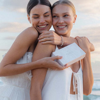 Zwei Frauen umarmen sich, eine trägt ein PURELEI-Armband, die andere hält eine Geschenkbox.