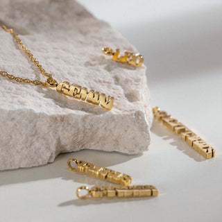 Goldene PURELEI Kette mit Buchstaben-Anhänger auf hellem Stein, elegant und modern.