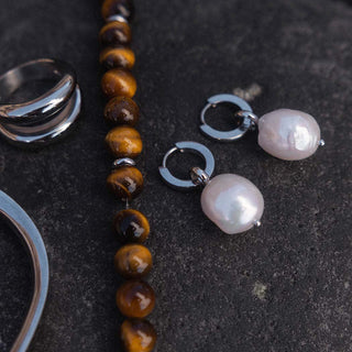 Silberne Ohrringe mit Perlen und braune Steinarmband von PURELEI auf dunklem Hintergrund.