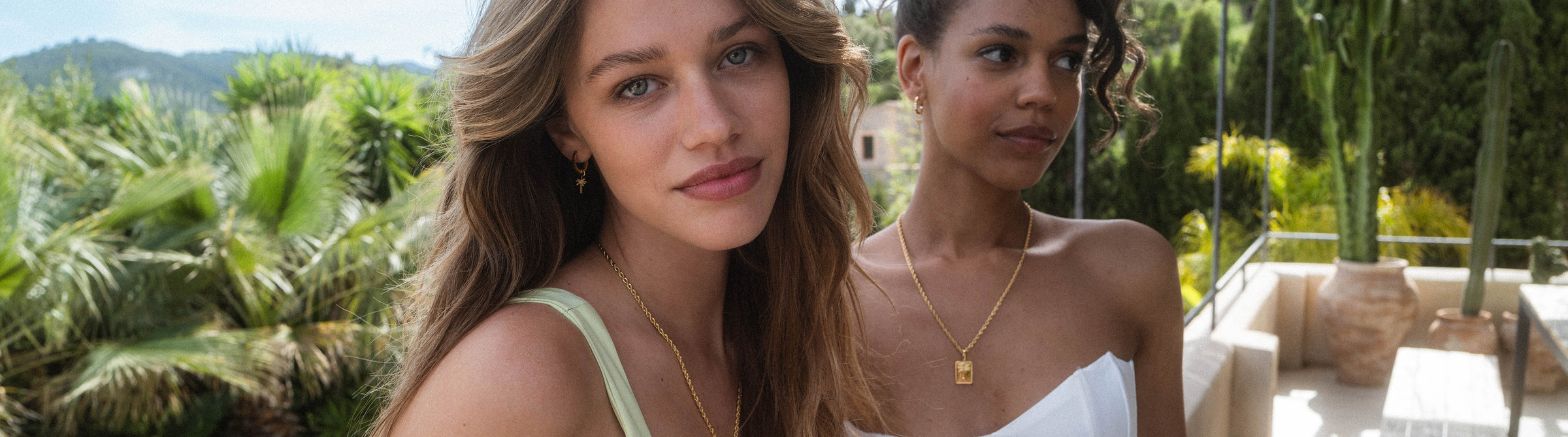 Zwei Frauen mit PURELEI Schmuck, goldene Kette und Ohrringe, umgeben von tropischer Natur.
