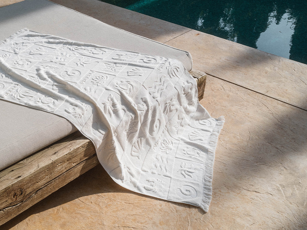 Weißes, strukturiertes Tuch von PURELEI auf einer Liege am Pool, mit tropischem Design.