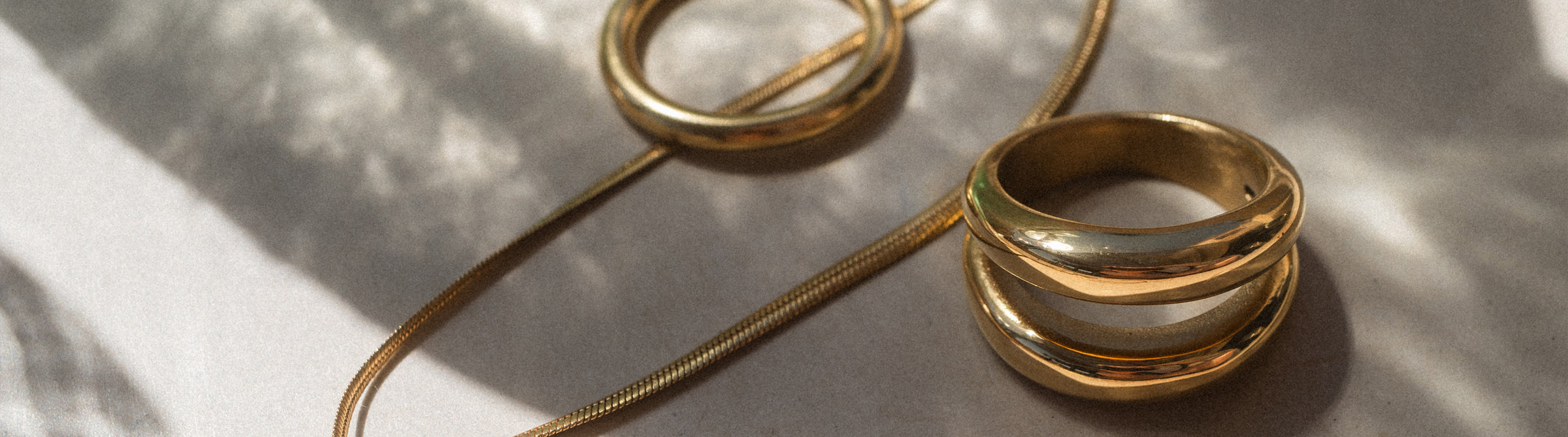 Goldene Ringe und Kette von PURELEI, elegant und zeitlos, in warmem Licht.