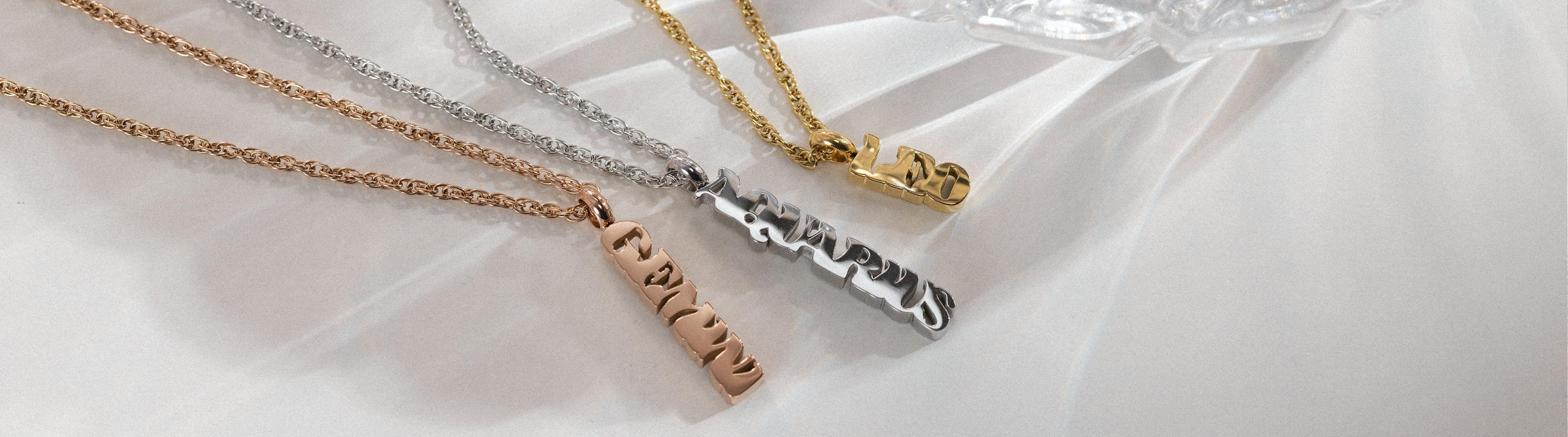 Drei personalisierte Ketten in Gold und Silber von PURELEI auf sanftem Hintergrund.