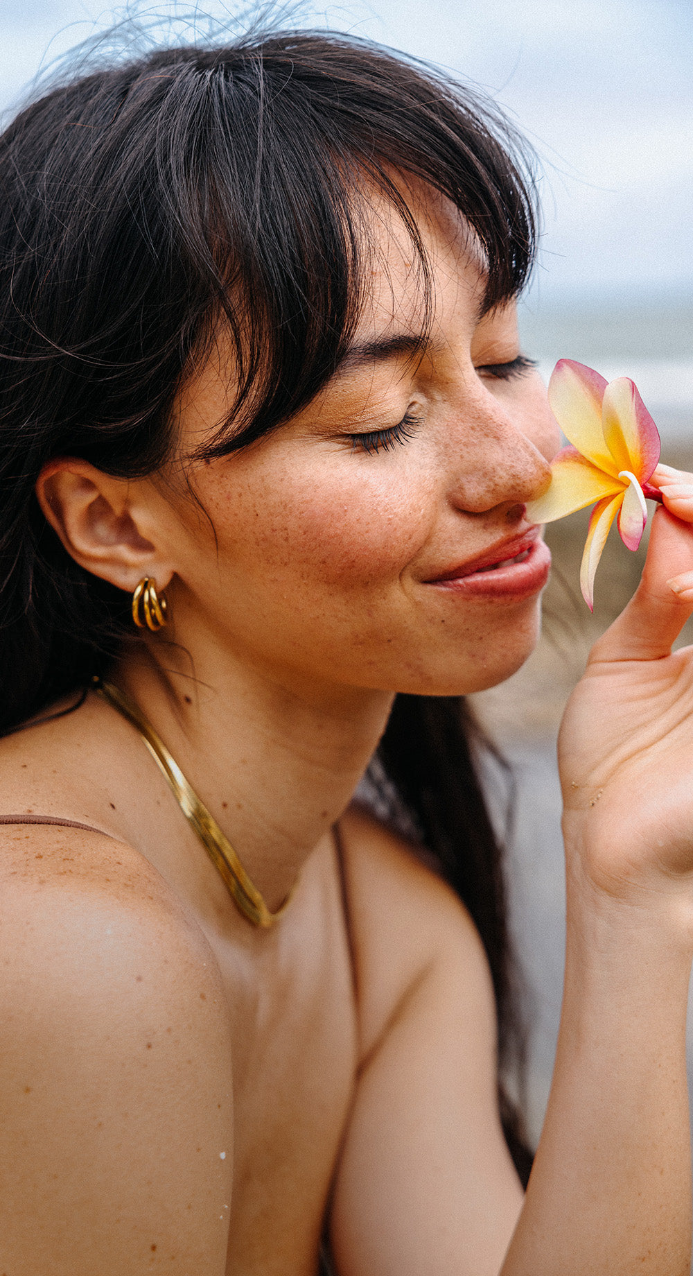 Goldene Creolen von PURELEI, getragen mit blühender Blume, strahlende, natürliche Eleganz.