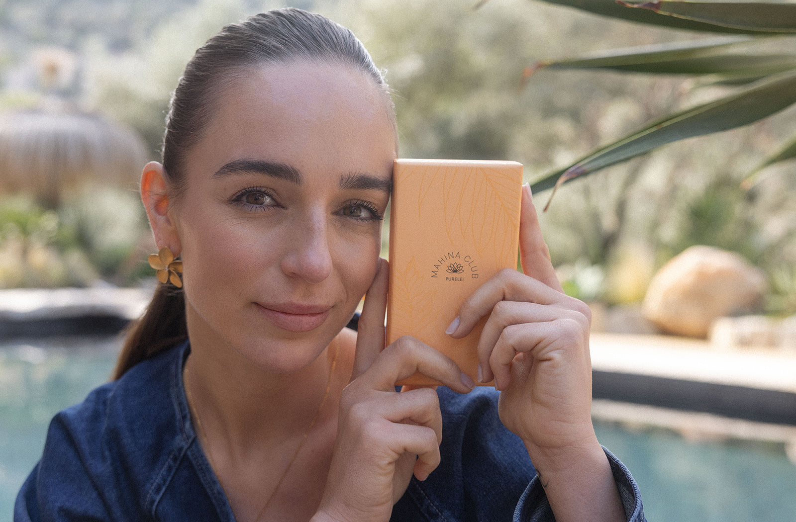 Frau hält orangefarbene Box mit PURELEI-Logo, umgeben von natürlicher Kulisse.