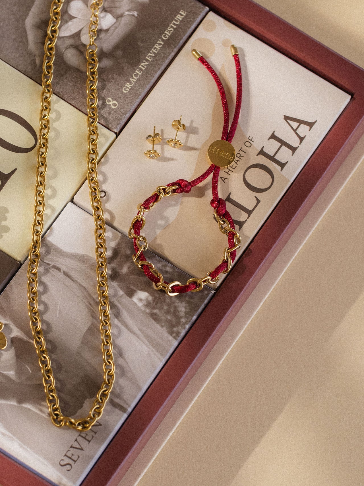 Goldene Kette und rotes Armband von PURELEI auf elegantem Hintergrund, inspiriert von Aloha.