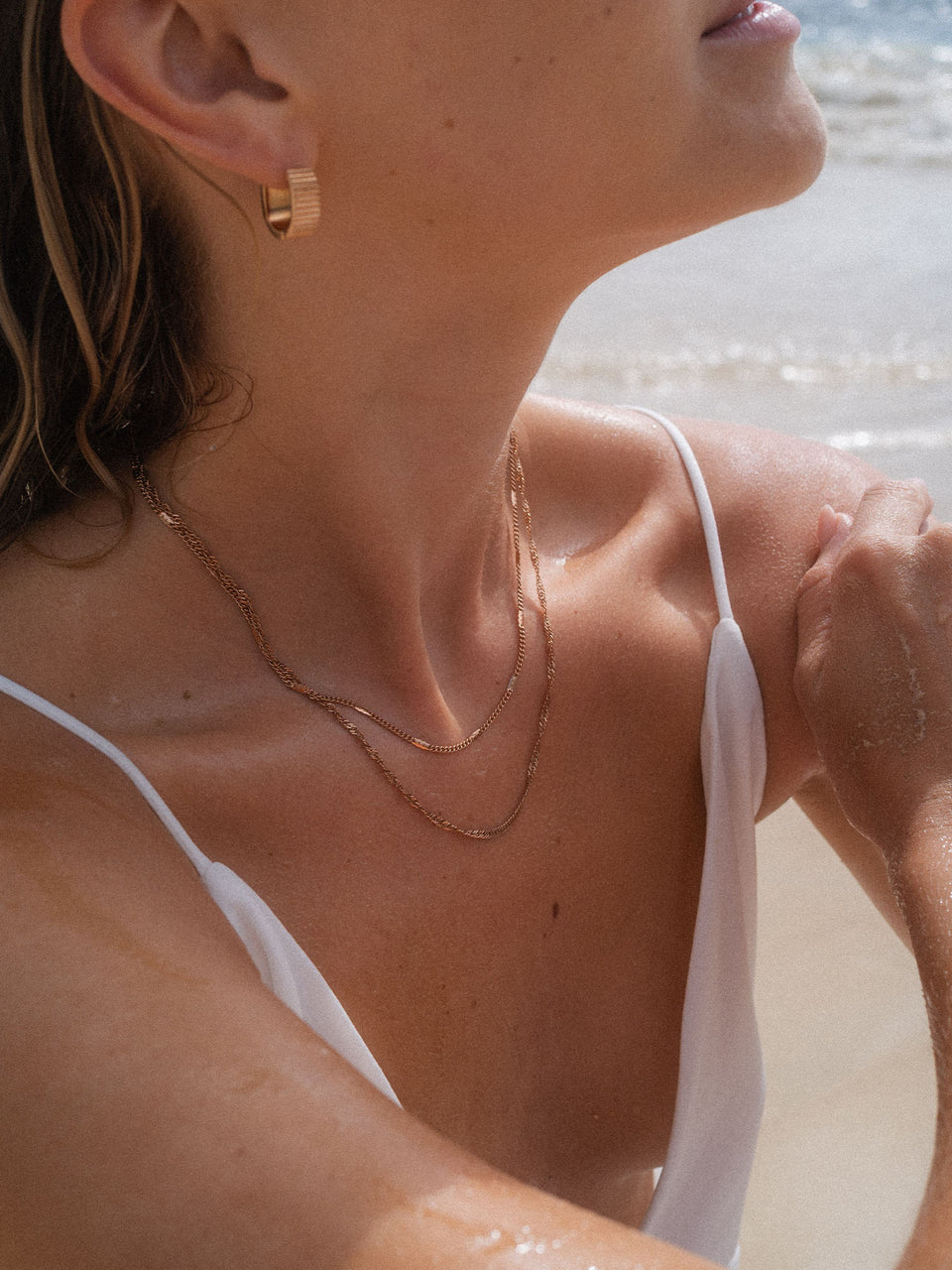 Zarte goldene Ketten und Creolen von PURELEI, elegant und beachy, am Strand getragen.