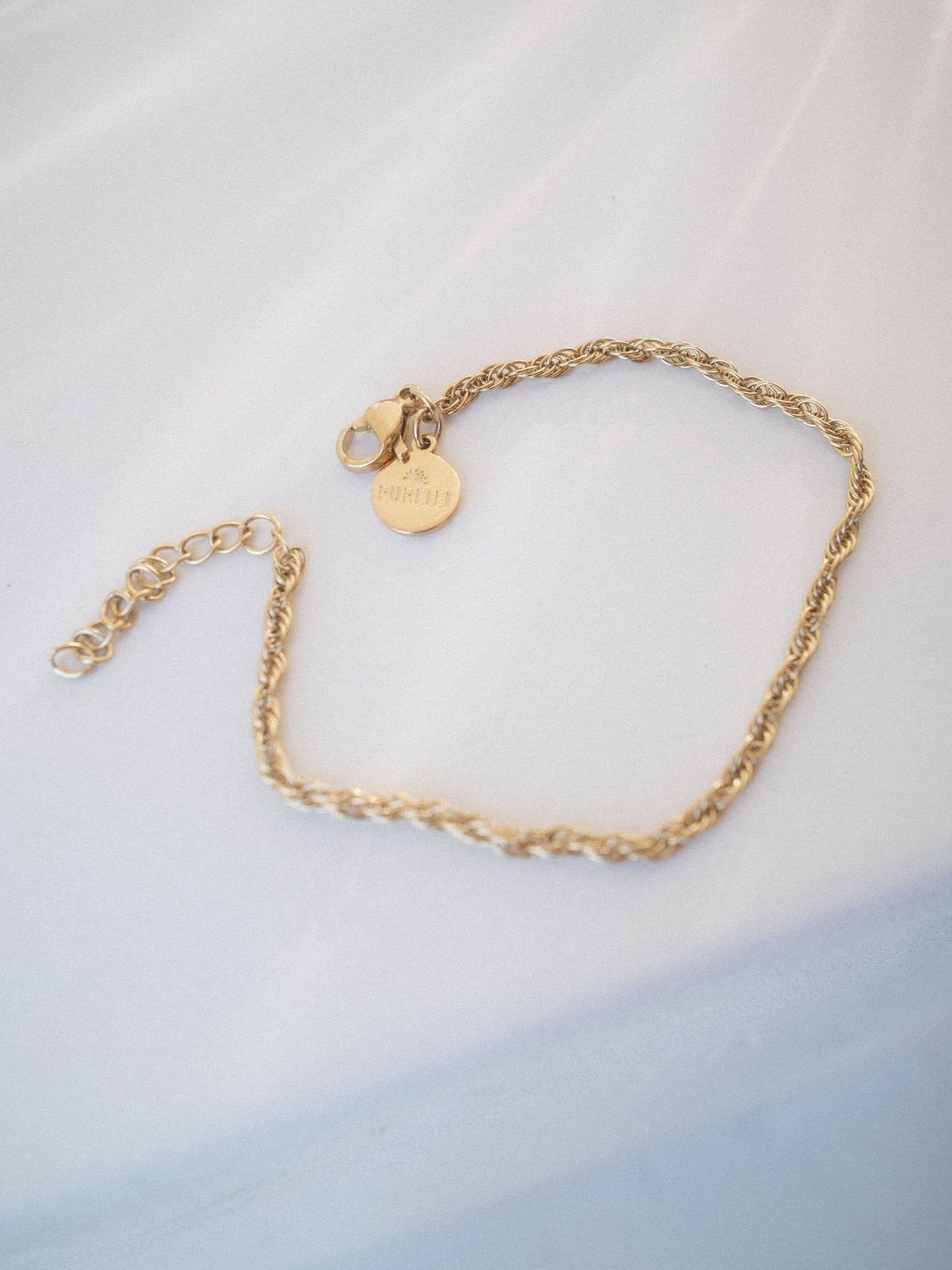 Goldene Kette mit geflochtenem Design und PURELEI-Anhänger auf hellem Hintergrund.