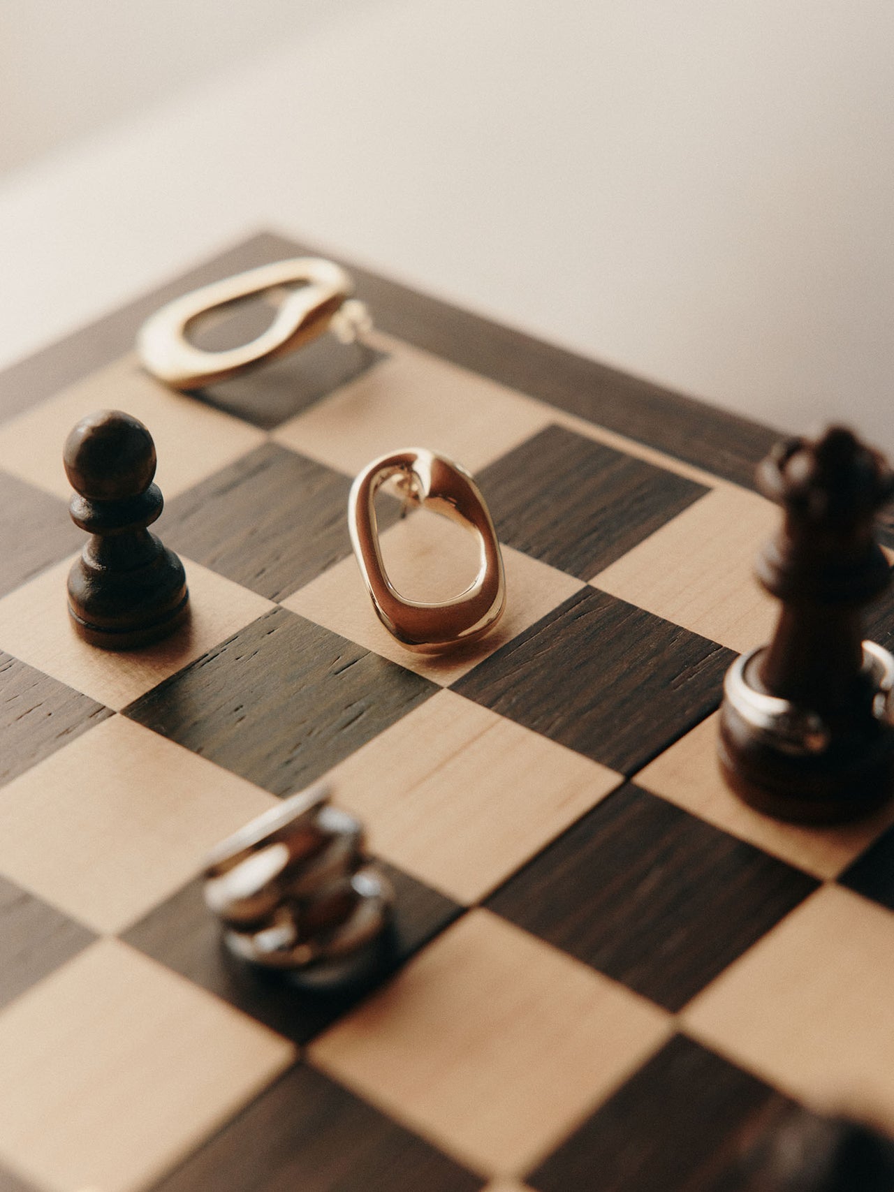 Silberne, organisch geformte Ohrringe auf einem Schachbrett, PURELEI inspiriert.