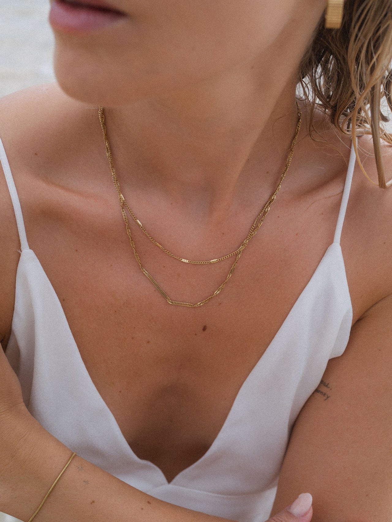 Zarte, roségoldene Kette von PURELEI, elegant geschichtet, getragen mit weißem Top.