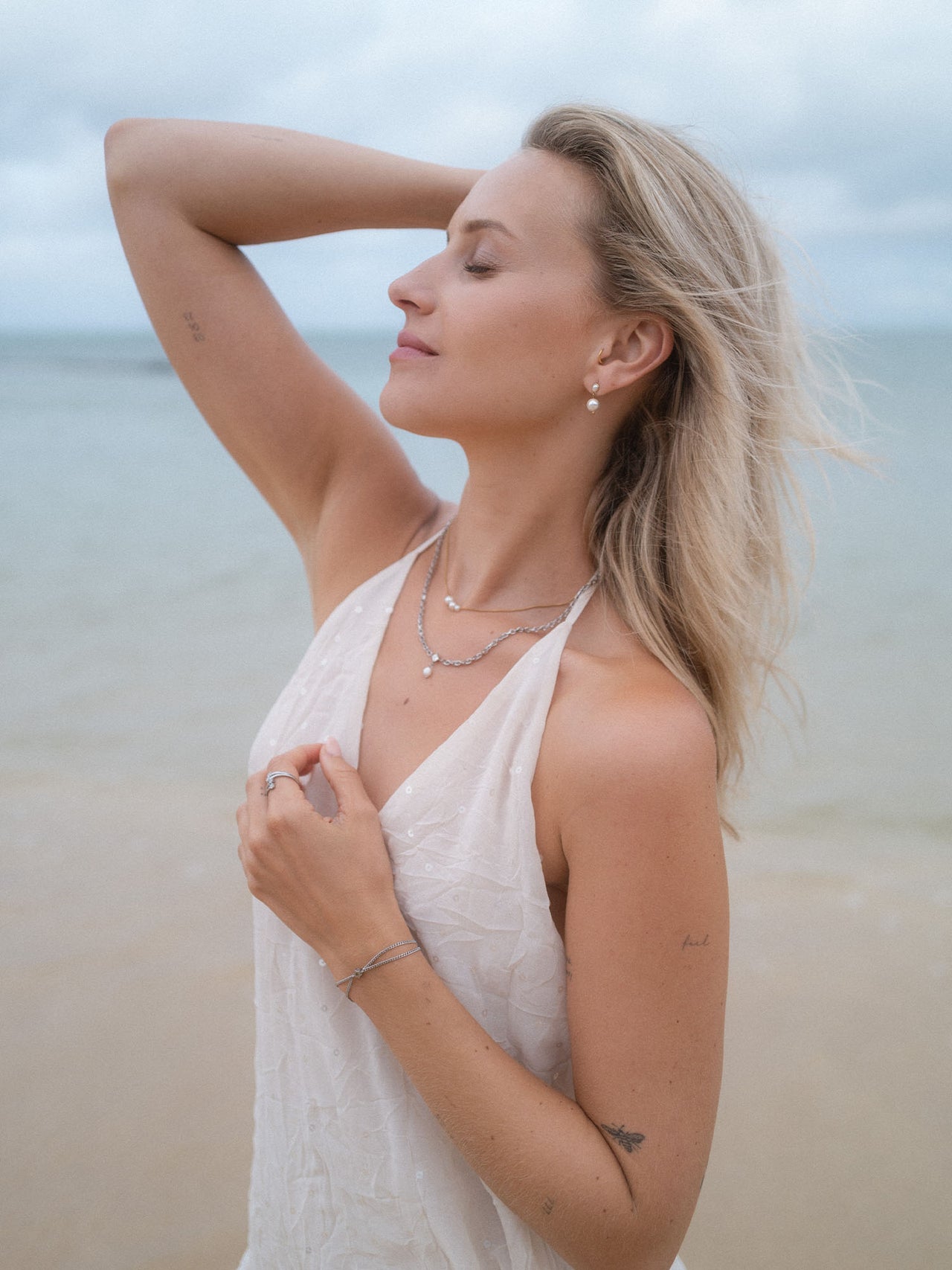 Elegante PURELEI Schmuckstücke in Silber, getragen am Strand mit sanften Wellen im Hintergrund.