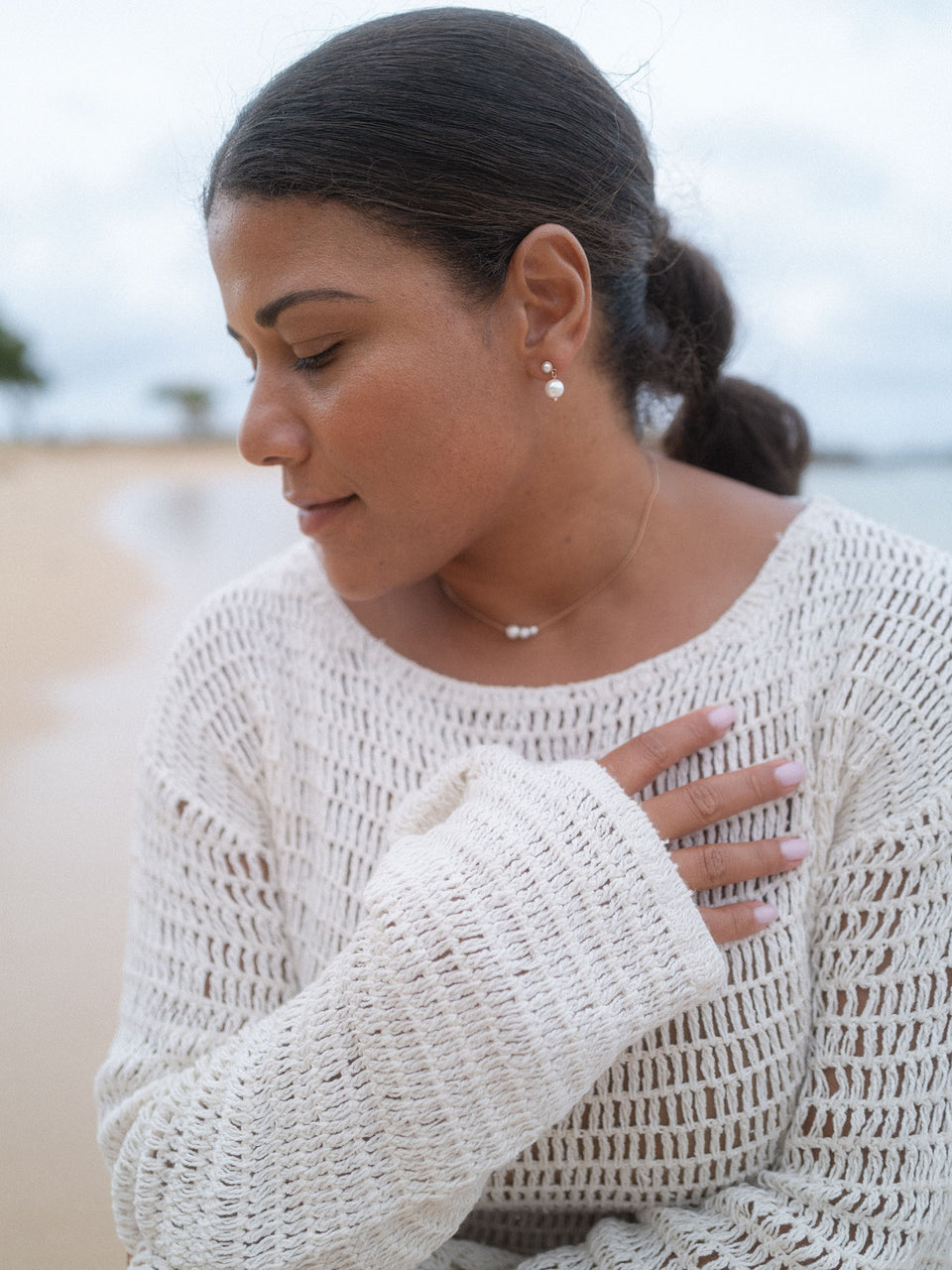 Elegante PURELEI Perlenohrringe, getragen am Strand, in sanften, natürlichen Tönen.