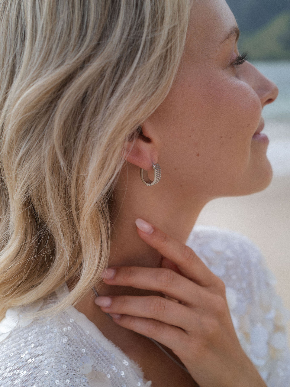 Silberne Creolen mit feiner Struktur, getragen von einer Frau am Strand, PURELEI.