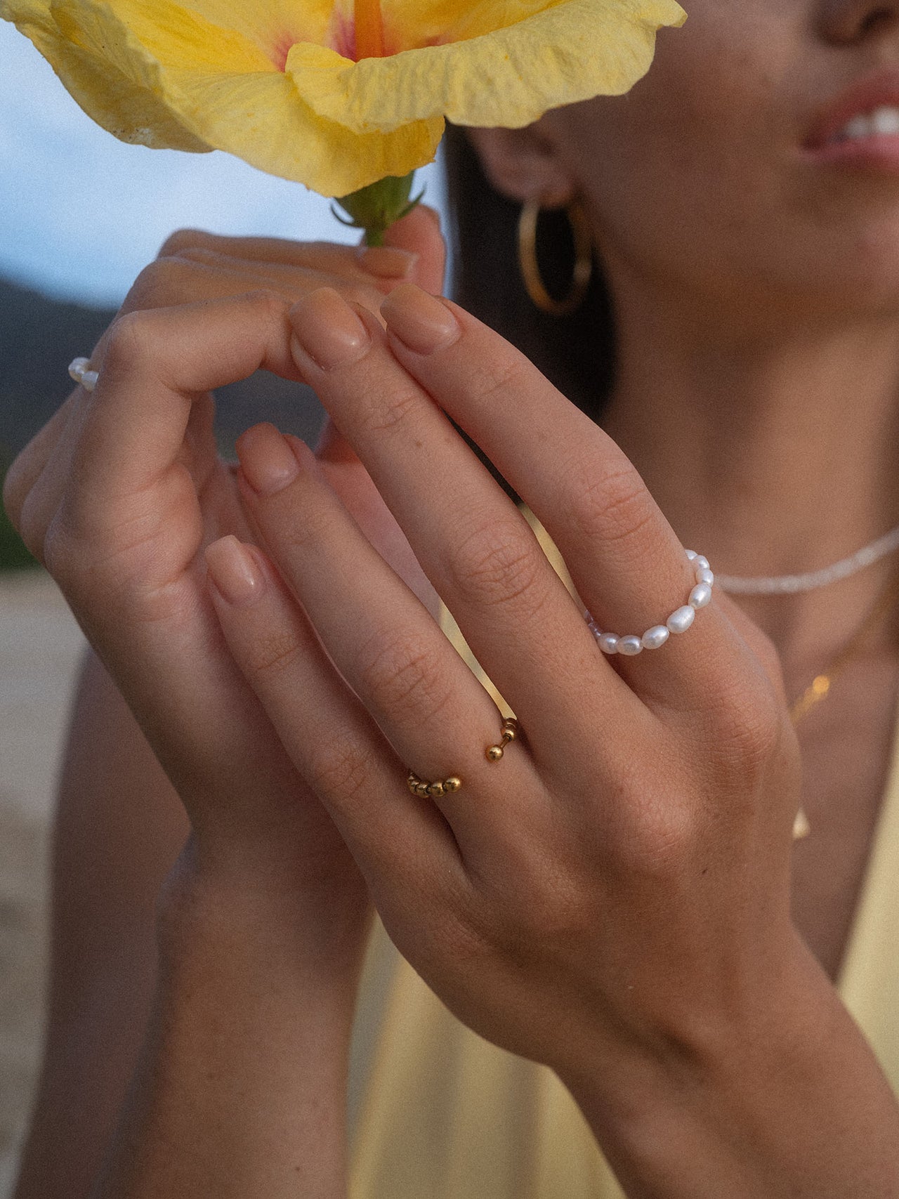 Goldene Ringe und Perlenarmband von PURELEI, elegant und feminin, umgeben von warmem Licht.