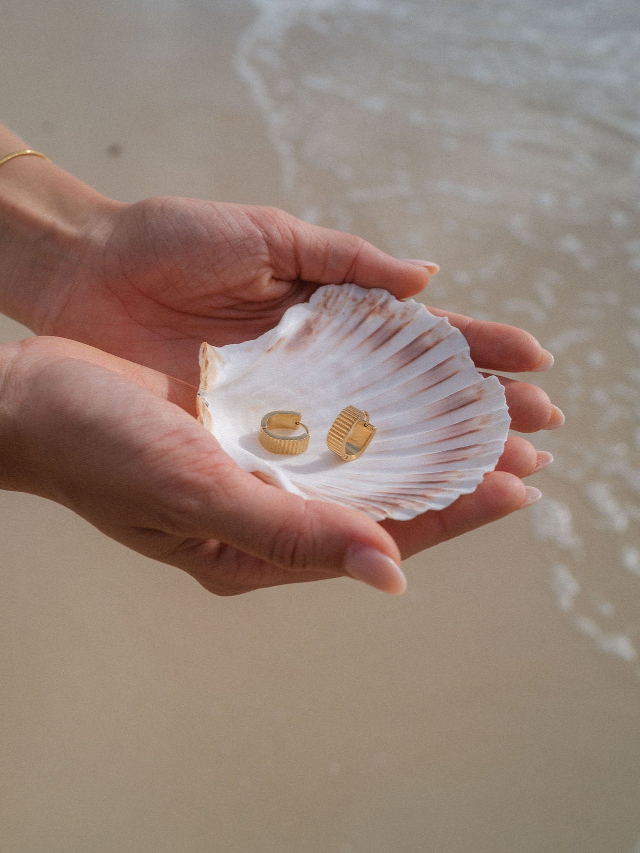 Zarte Ohrringe in Muschel auf Hand, PURELEI inspiriert von tropischer Eleganz.