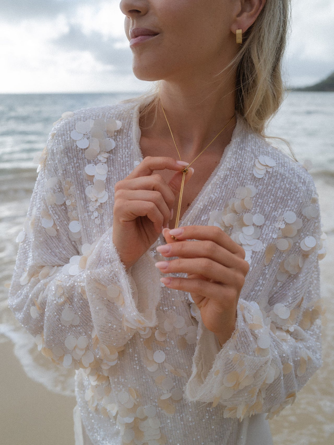 Silberne Kette und Ohrringe von PURELEI, getragen am Strand, mit glitzerndem Oberteil.