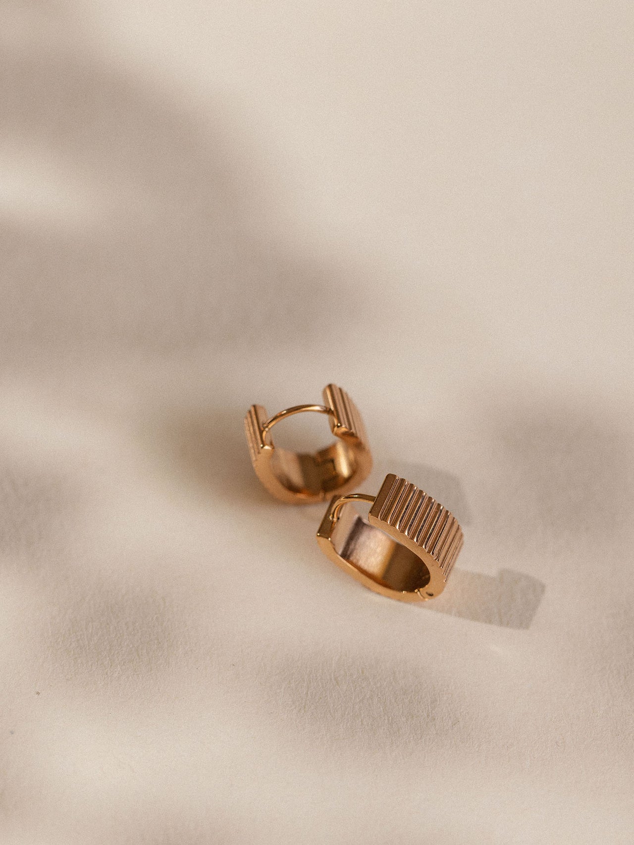 Goldene Creolen mit strukturiertem Design auf sanftem Hintergrund – PURELEI.