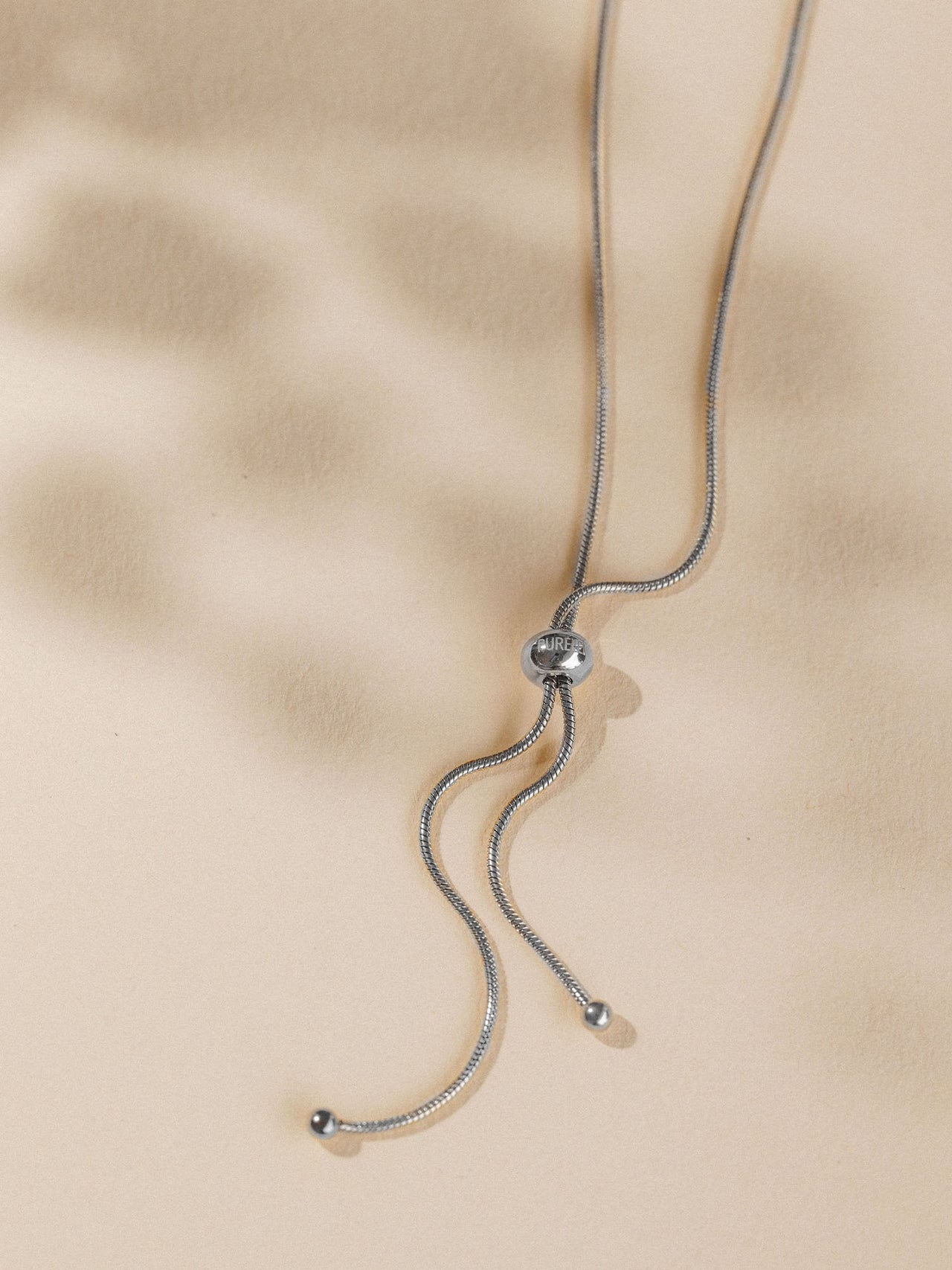 Silberne Kette mit geschwungenem Design, PURELEI, elegant auf beigem Hintergrund.