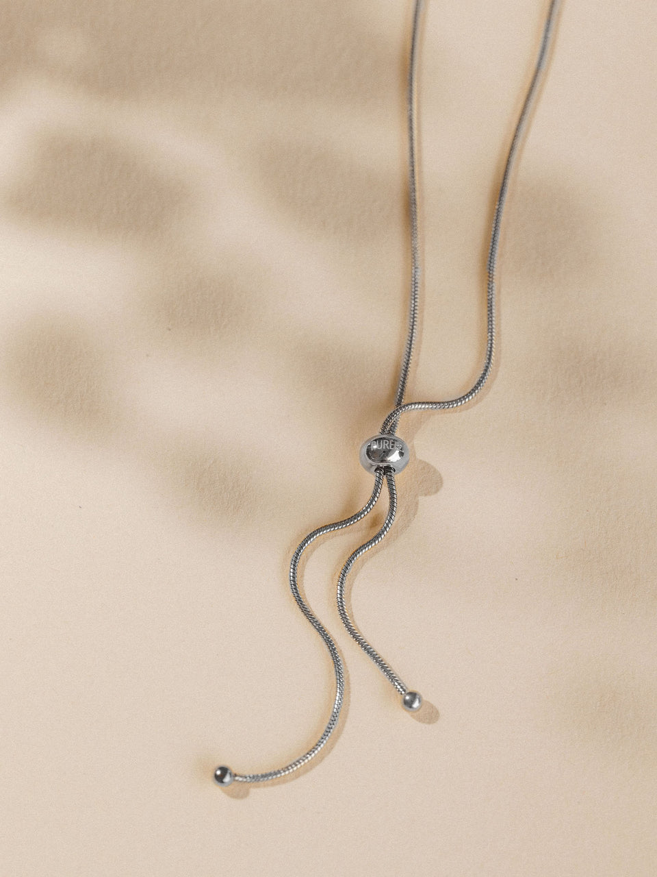 Silberne Kette mit geschwungenem Design, PURELEI, elegant auf beigem Hintergrund.