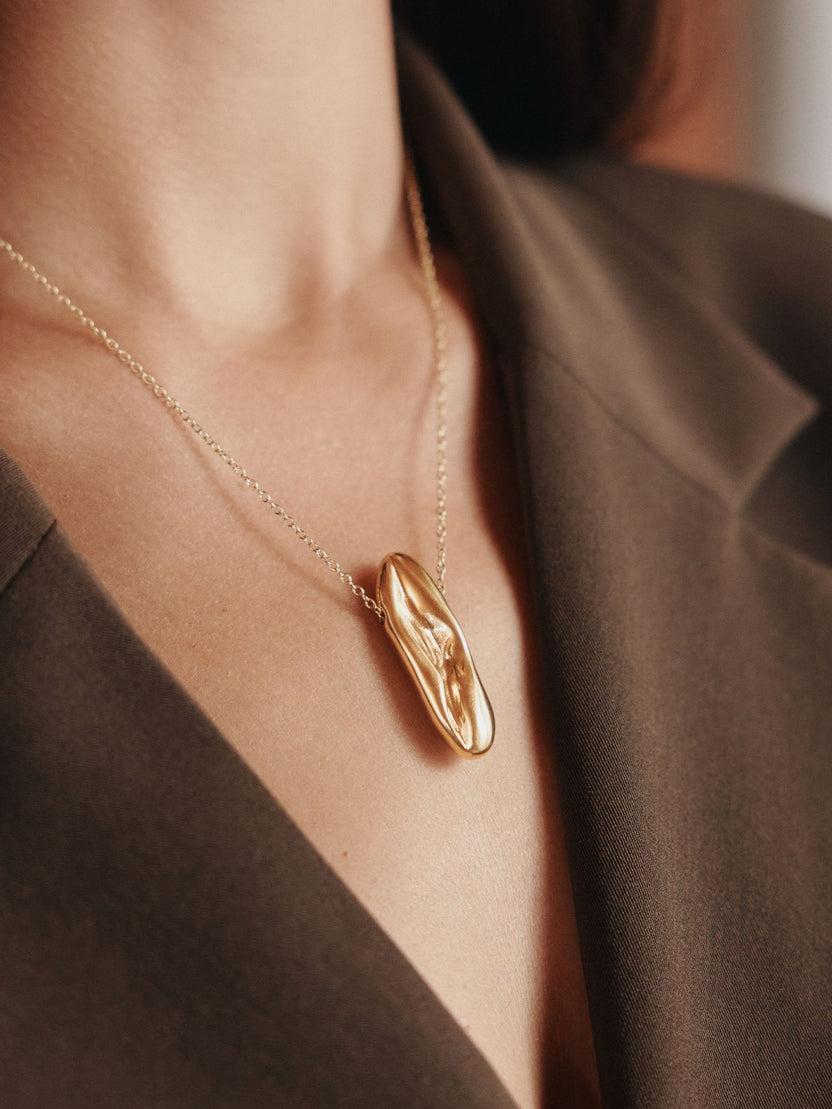 Elegante, roségoldene Kette mit geschwungenem Anhänger von PURELEI, getragen auf einem dunklen Oberteil.