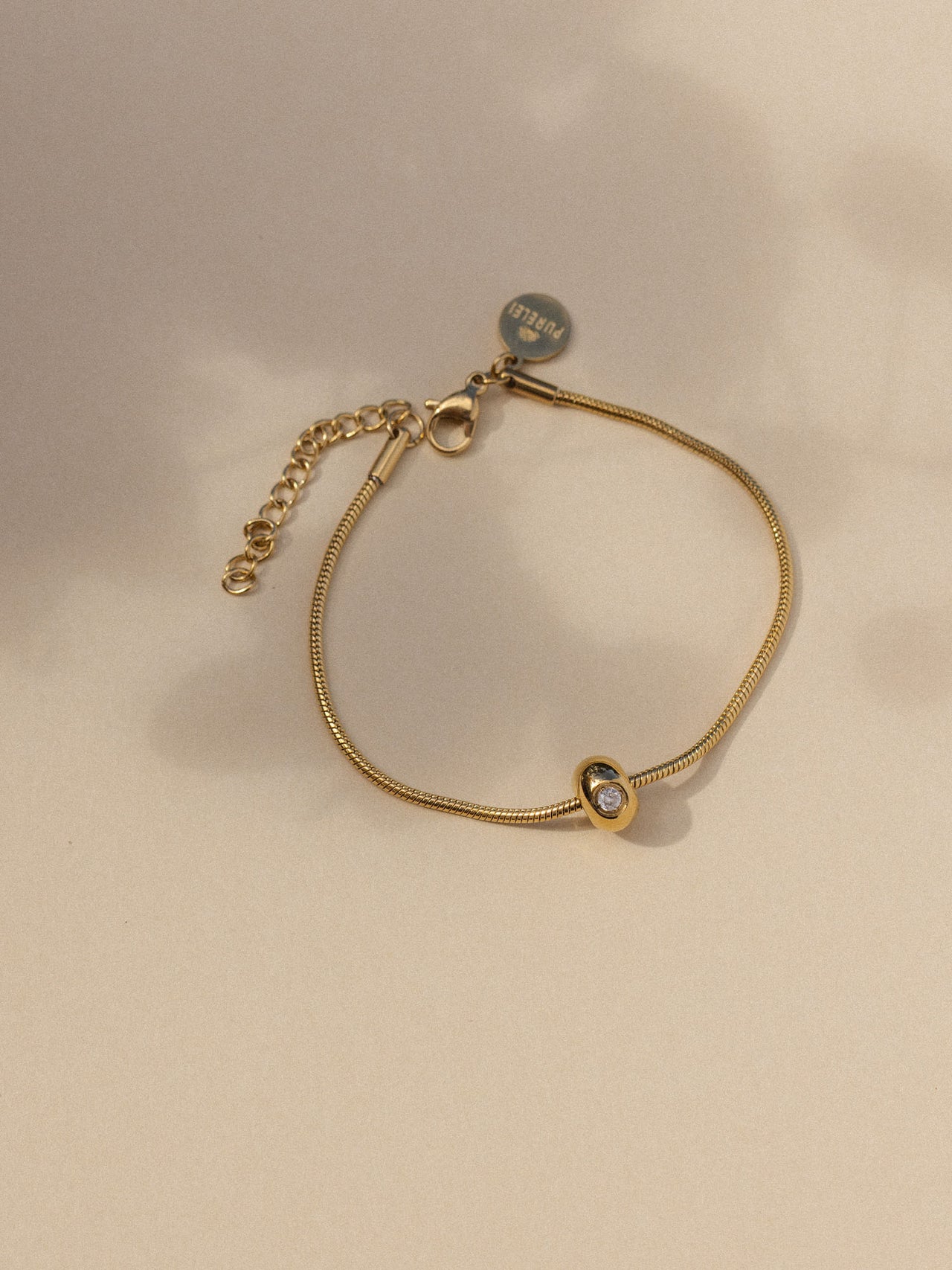 Elegantes, goldenes Armband mit funkelndem Detail von PURELEI, auf sanftem Hintergrund.