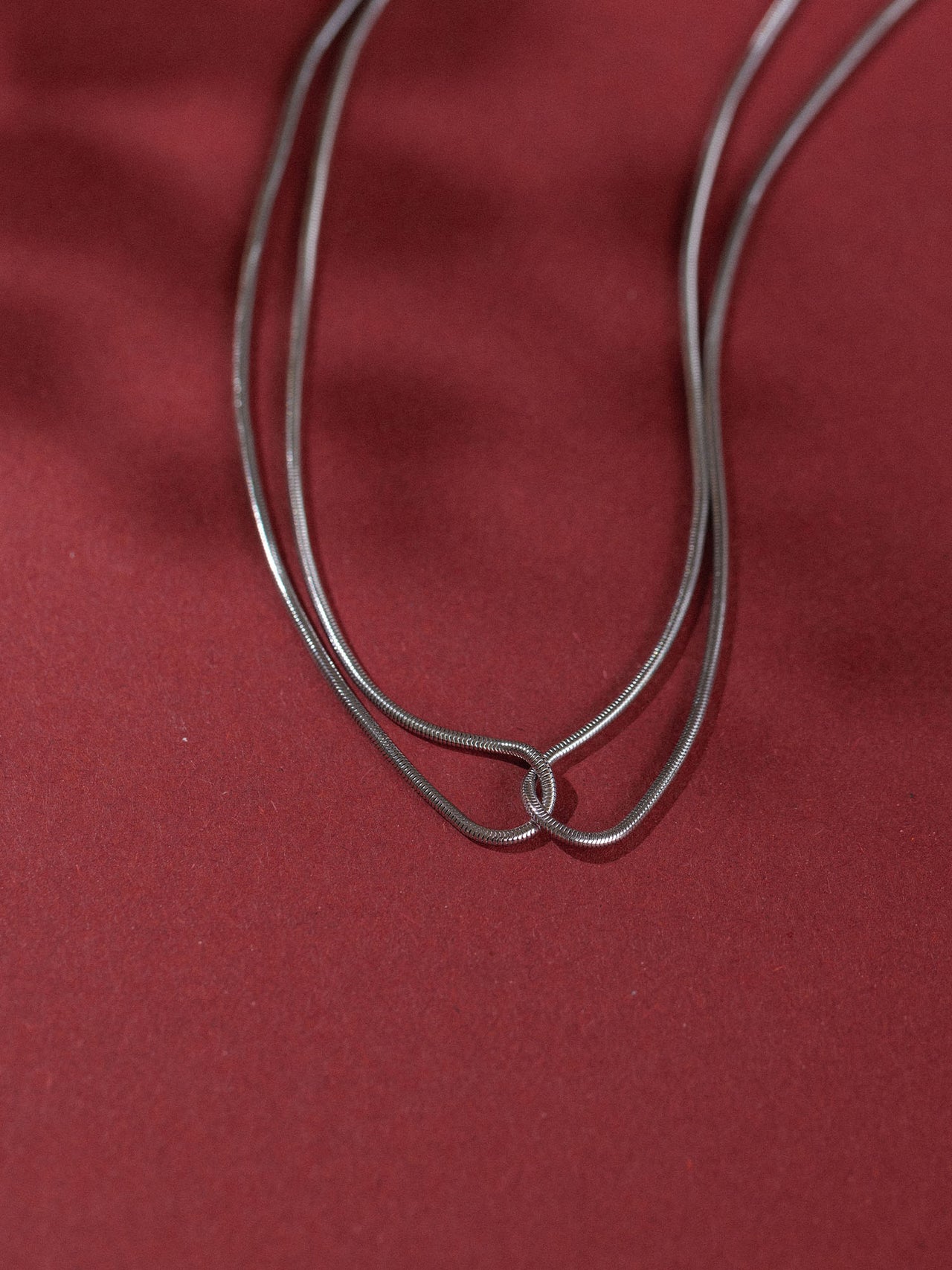 Doppelte, rote Kette von PURELEI auf rotem Hintergrund, elegant und schlicht.