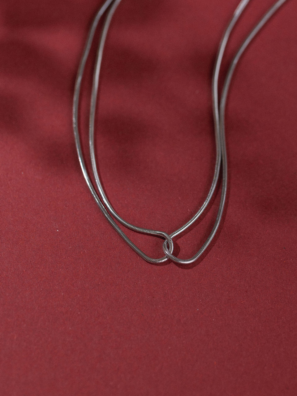 Doppelte, rote Kette von PURELEI auf rotem Hintergrund, elegant und schlicht.