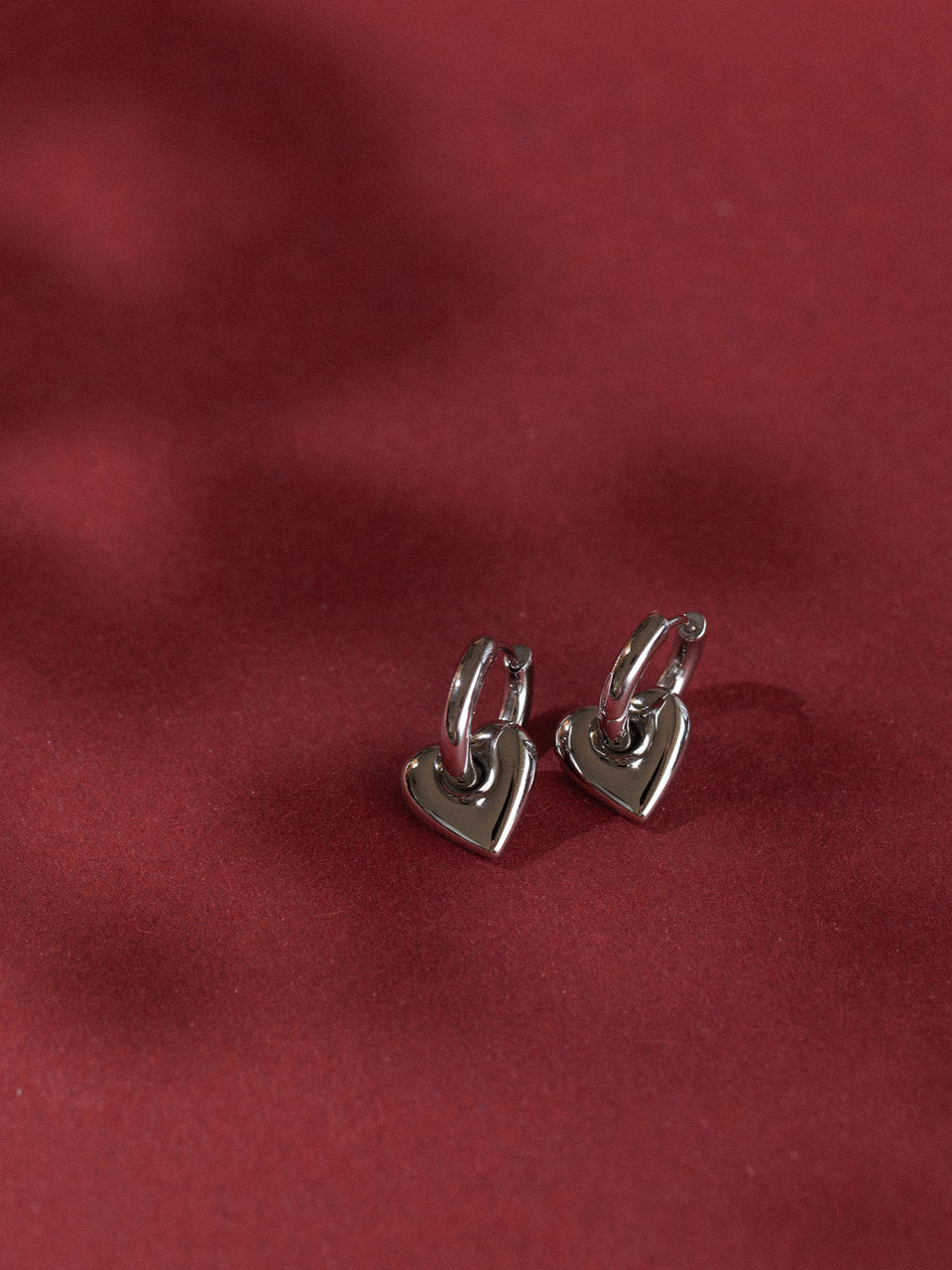 Herzförmige Ohrringe aus rosegold, elegant auf rotem Hintergrund, PURELEI.