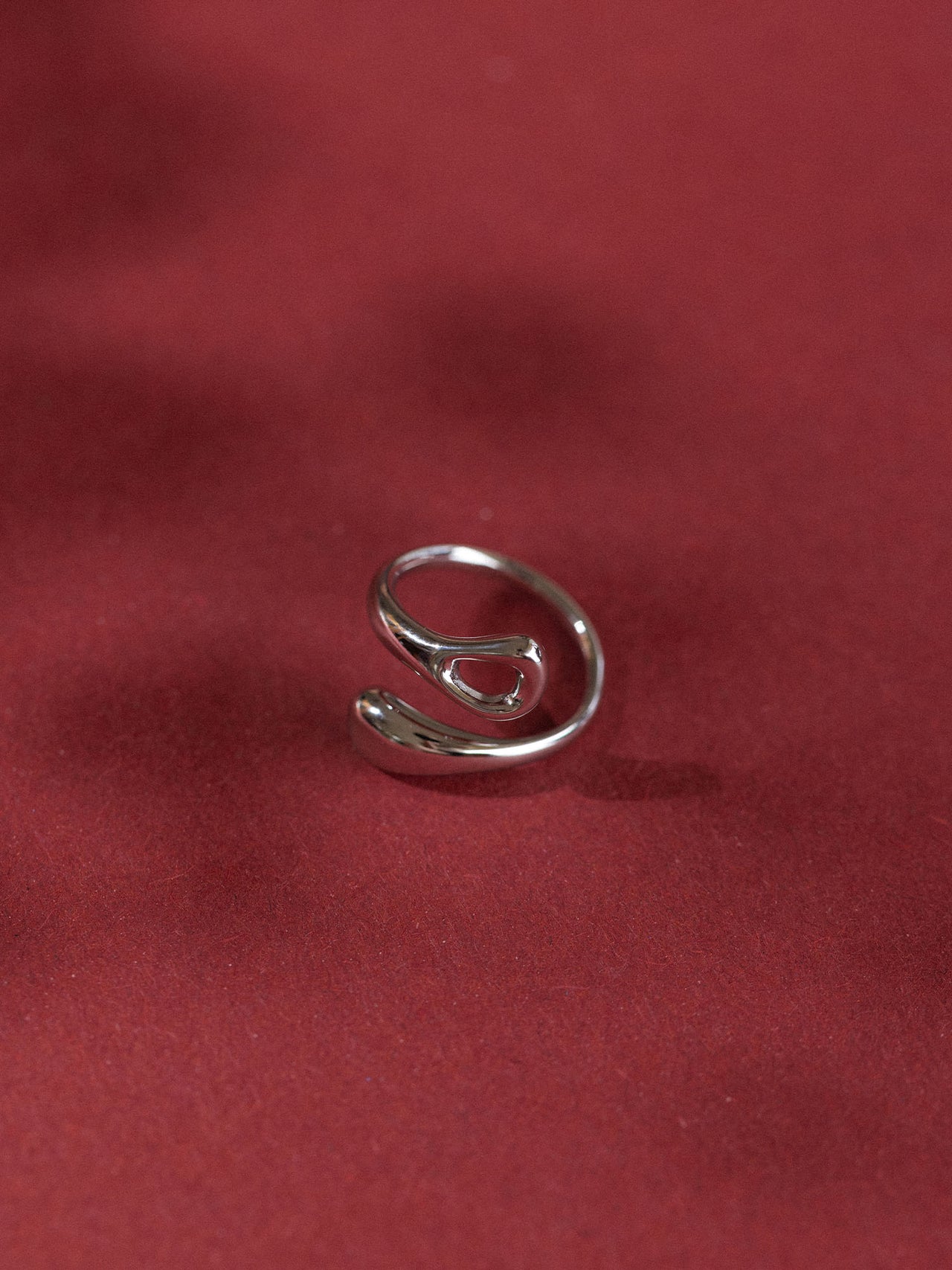 Eleganter, roter Ring von PURELEI mit geschwungenem Design auf rotem Hintergrund.