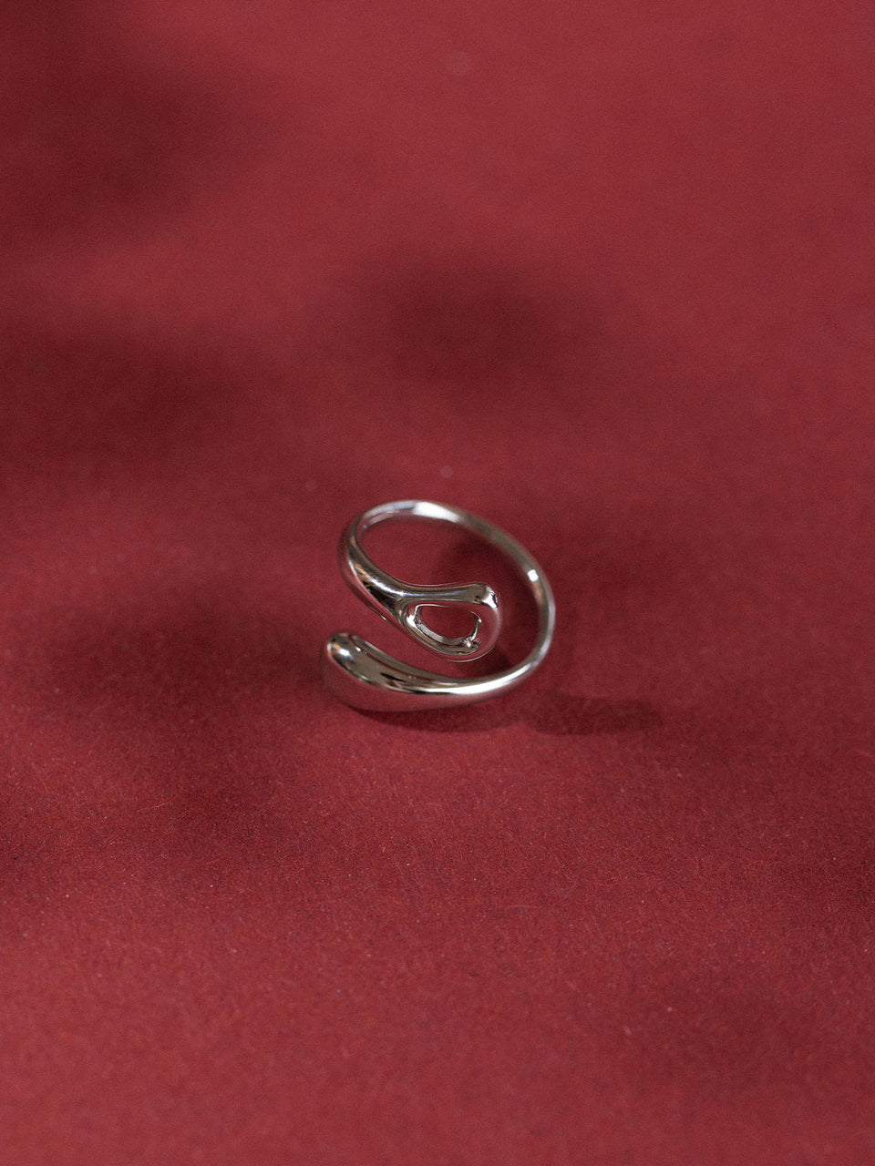 Eleganter, roter Ring von PURELEI mit geschwungenem Design auf rotem Hintergrund.