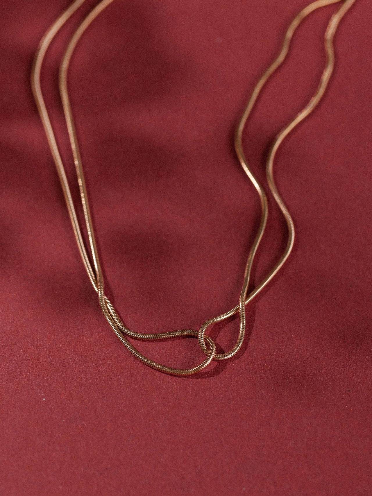 Zweifädige, roségoldene Kette auf rotem Hintergrund, elegant und modern – PURELEI.