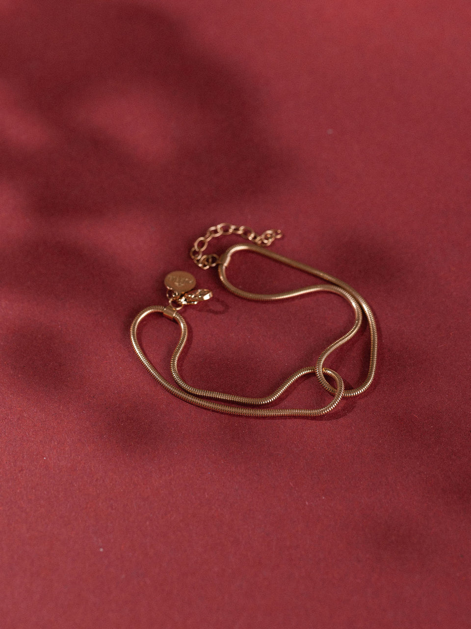 Roségoldene Kette mit zarten Anhängern auf rotem Hintergrund von PURELEI.