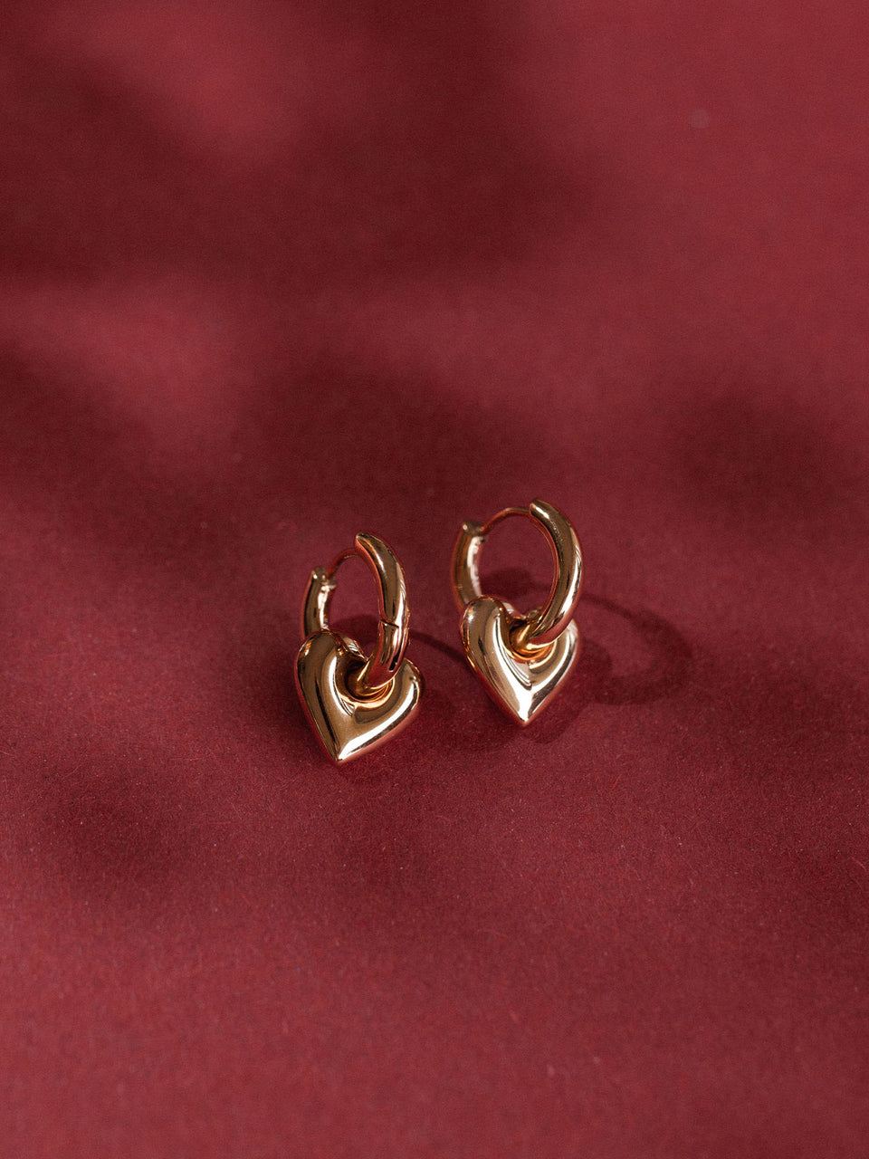 Herzförmige, roségoldene Ohrringe von PURELEI auf rotem Hintergrund, elegant und verspielt.