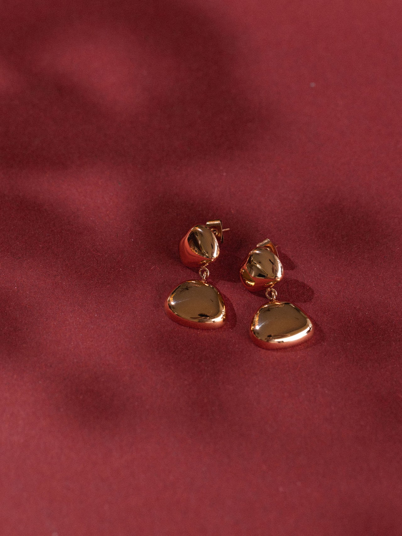 Elegante, roségoldene Ohrringe mit geschwungenem Design von PURELEI auf rotem Hintergrund.