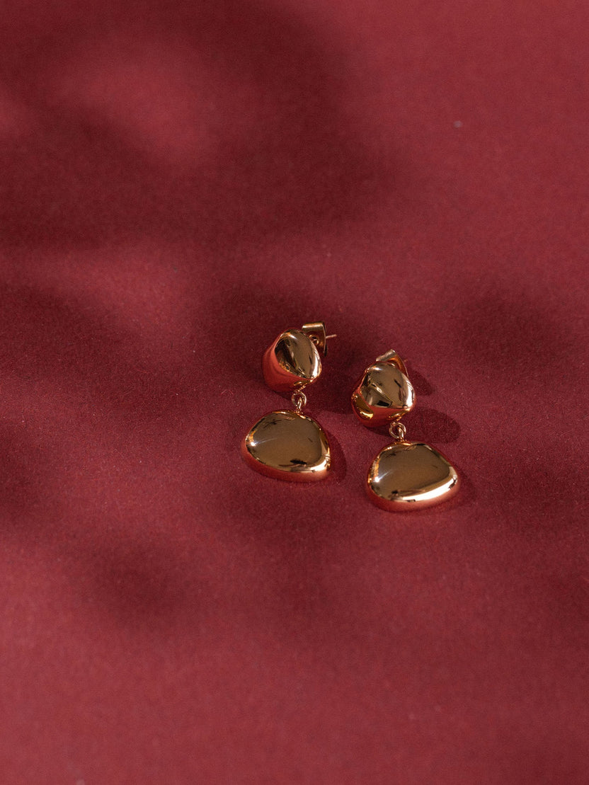 Elegante, roségoldene Ohrringe mit geschwungenem Design von PURELEI auf rotem Hintergrund.