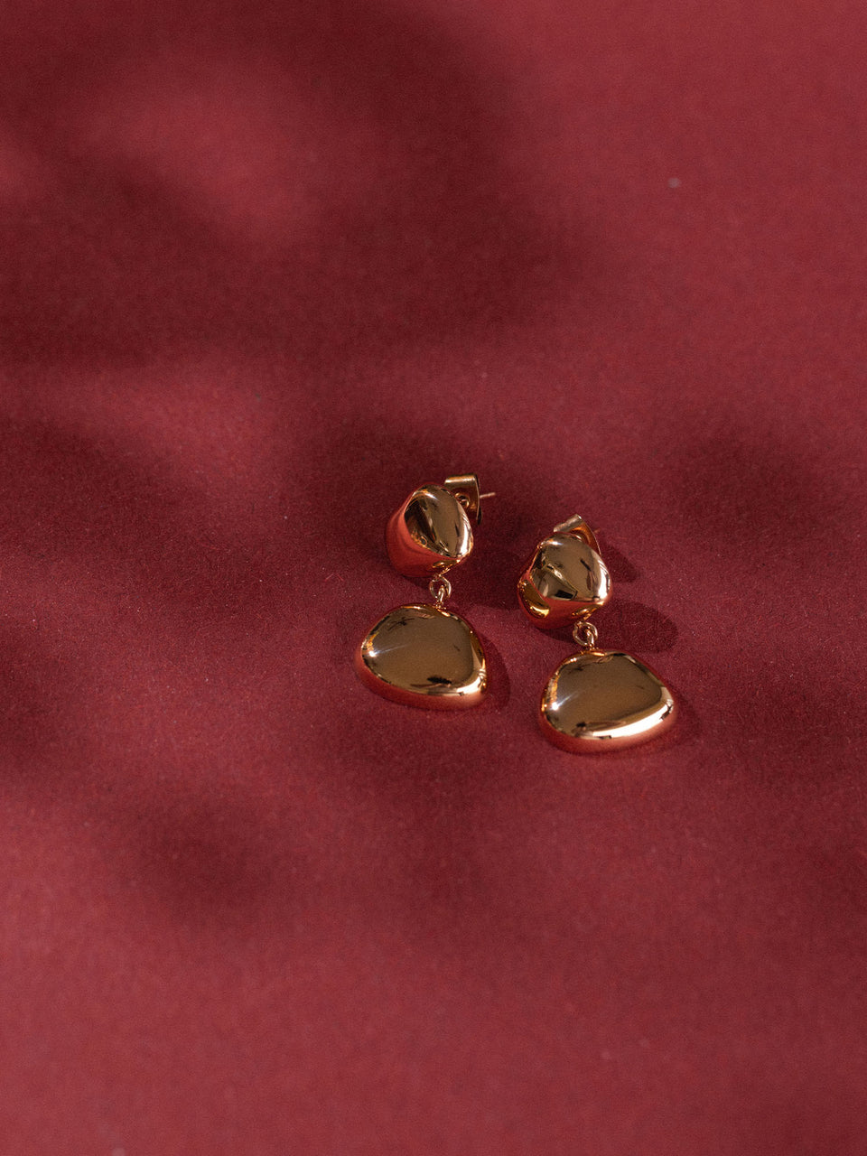 Elegante, roségoldene Ohrringe mit geschwungenem Design von PURELEI auf rotem Hintergrund.