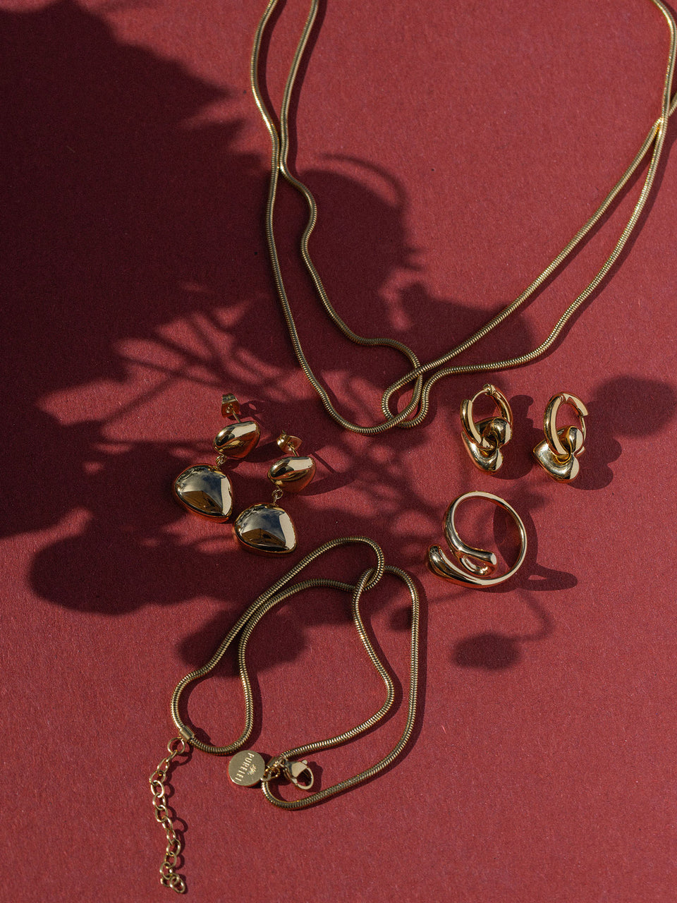 Elegante, roségoldene Schmuckstücke von PURELEI auf rotem Hintergrund, strahlend und modern.