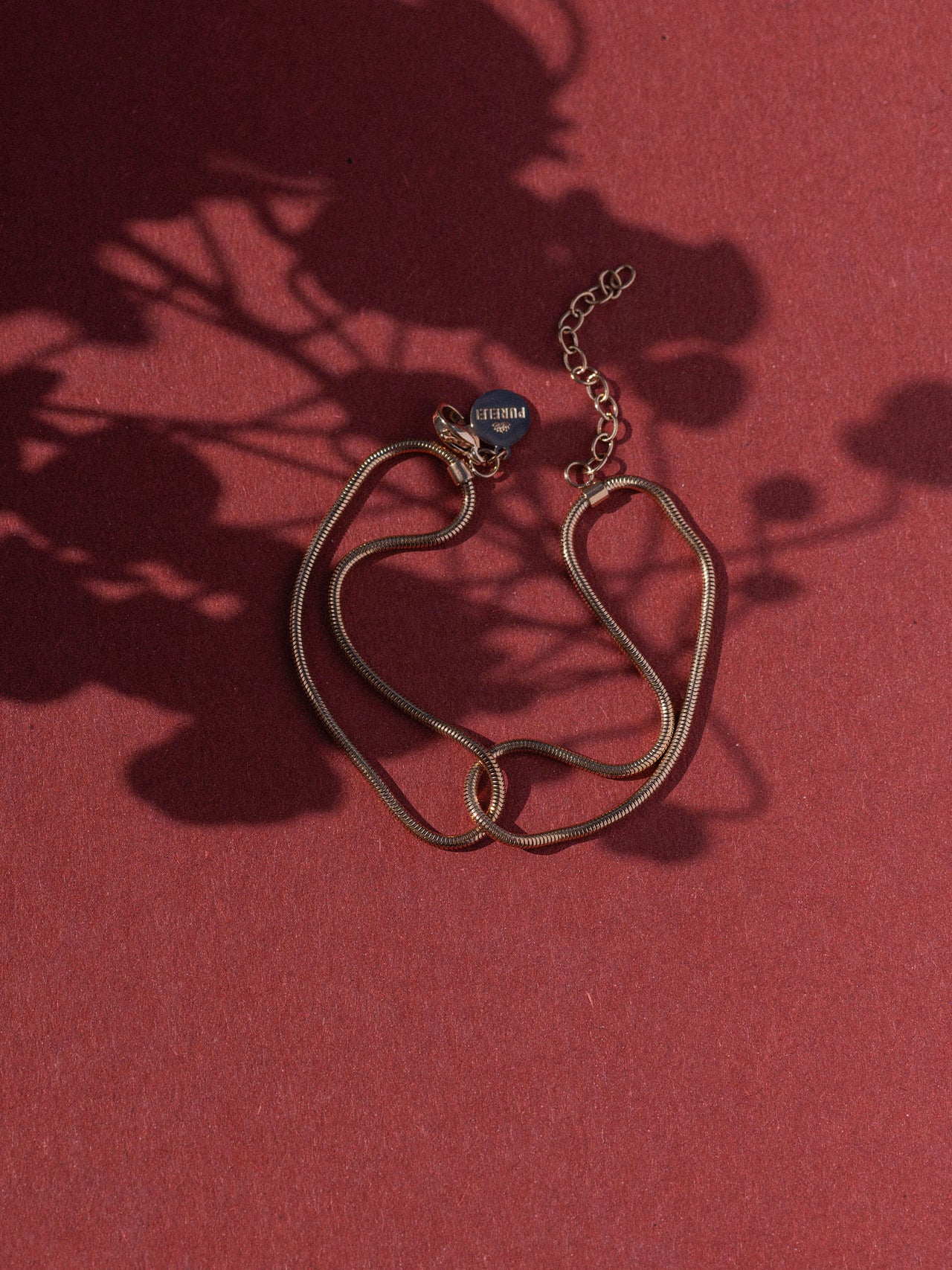 Dunkelrotes, elegantes Armband von PURELEI mit geschwungenem Design auf rotem Hintergrund.