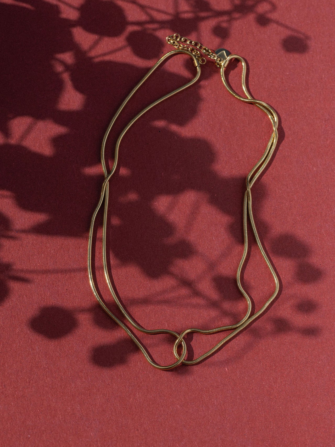 Braune Kette mit elegantem Design auf rotem Hintergrund, inspiriert von PURELEI.
