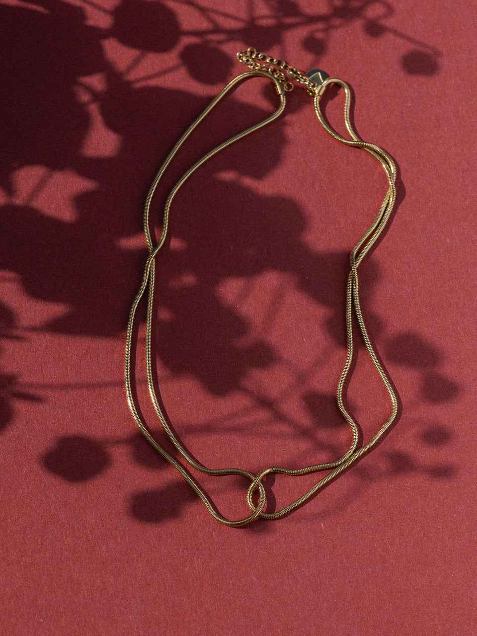Braune Kette mit elegantem Design auf rotem Hintergrund, inspiriert von PURELEI.