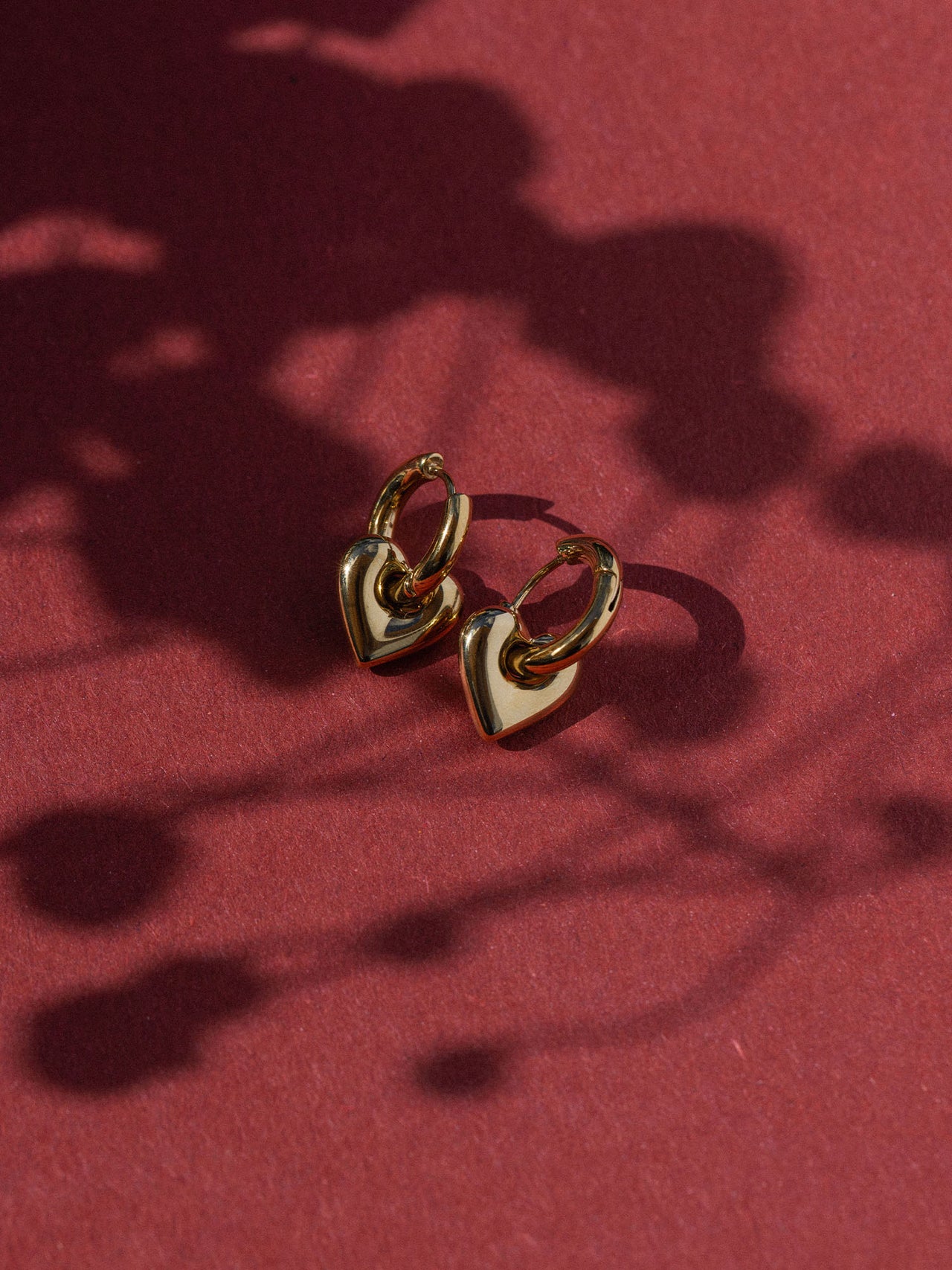 Dunkelrote Creolen mit Herzdesign auf rotem Hintergrund, PURELEI Schmuck für feminine Eleganz.