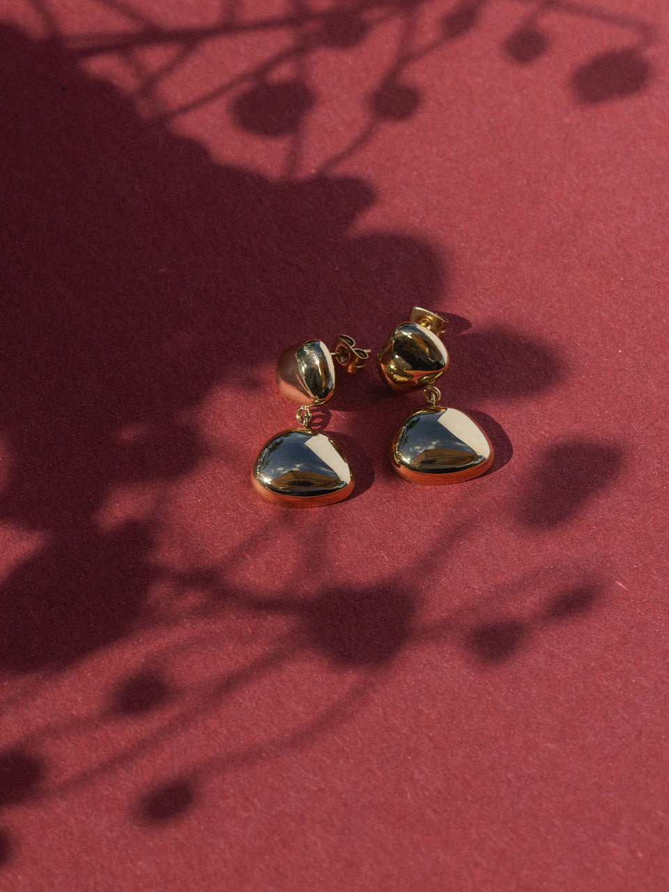 Silberne Ohrringe mit tropfenförmigem Design auf rotem Hintergrund, PURELEI inspiriert.