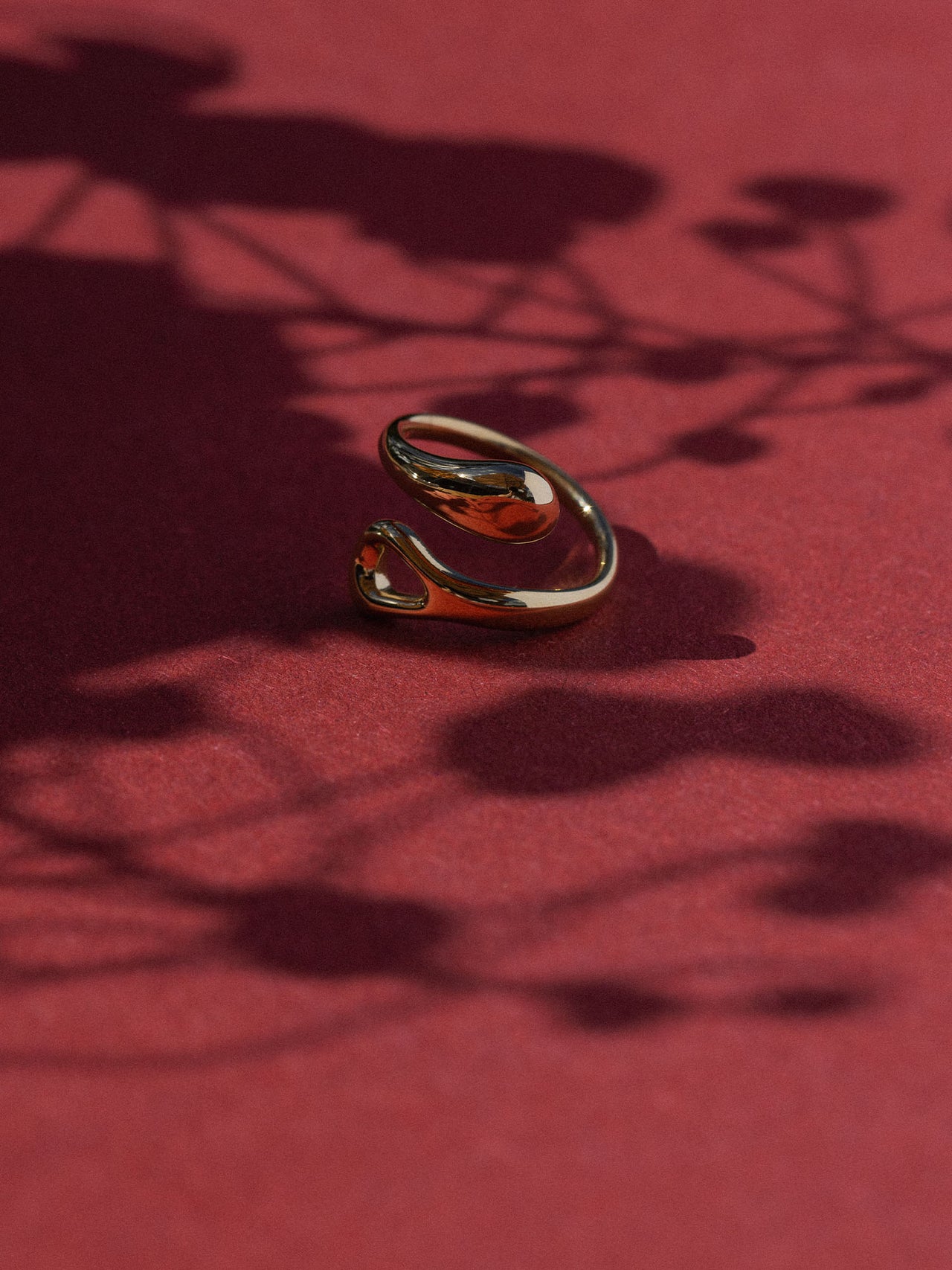 Eleganter, geschwungener Ring aus glänzendem Metall auf rotem Hintergrund – PURELEI.