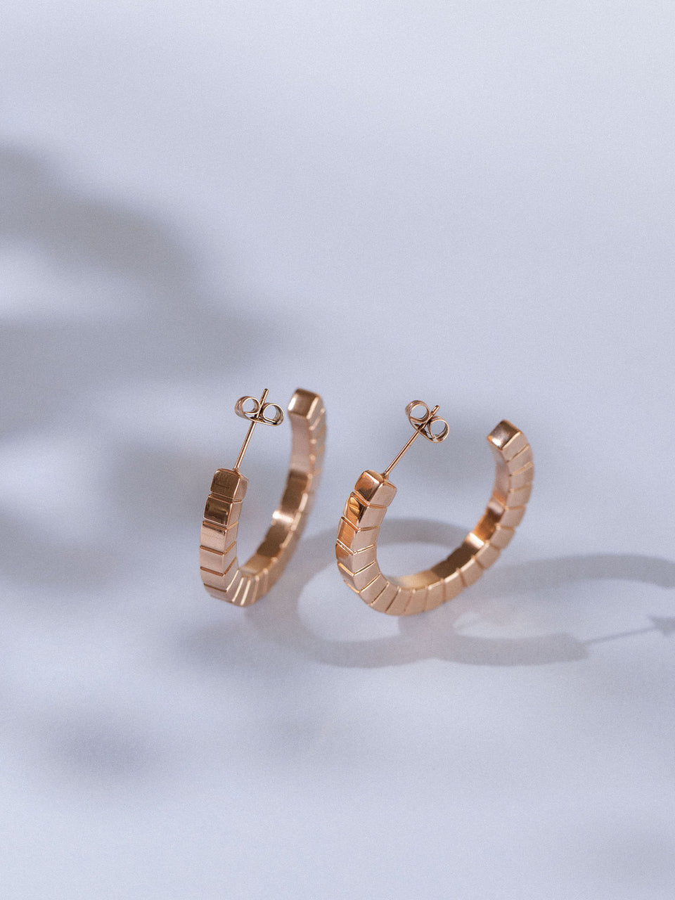 Roségoldene Creolen mit geometrischem Design von PURELEI auf sanftem Hintergrund.